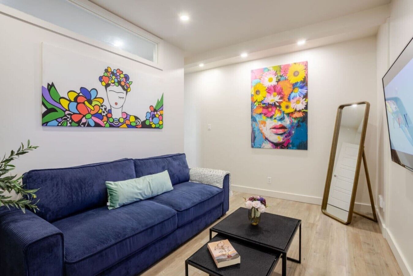 Une pièce avec un canapé bleu, une petite table noire sur laquelle se trouve un livre, et deux tableaux accrochés au mur.