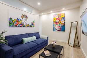 A room with a blue sofa, a small black table with a book, and two paintings on the wall. - Magnificent Apartment in Montréal (Montreal)