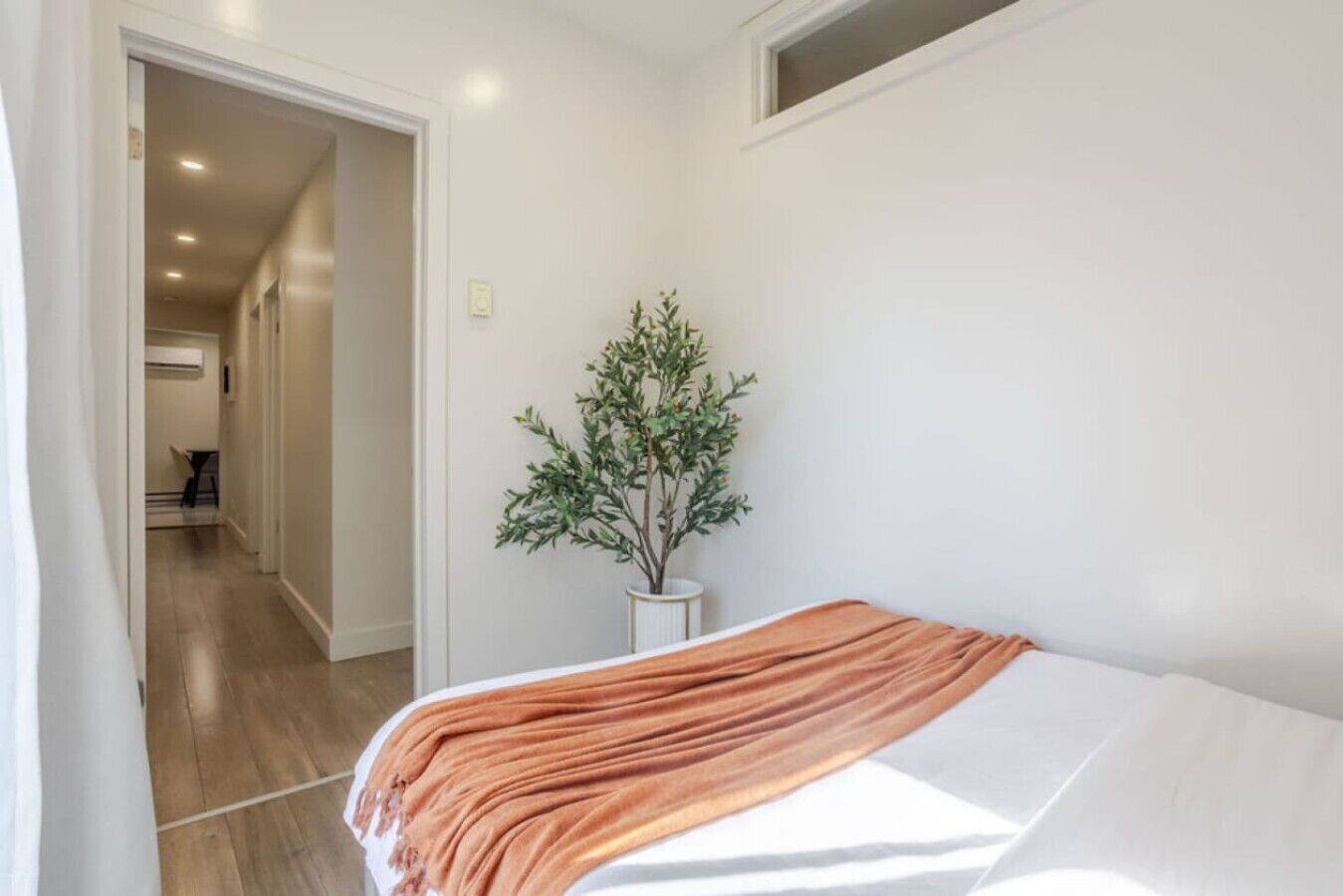 Een slaapkamer met een bed, een kamerplant en een gang naar een andere kamer.