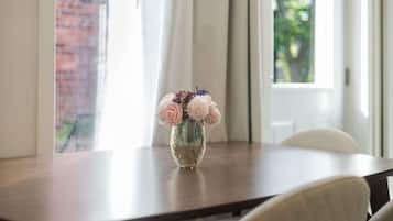 Ein Esstisch mit Blumen in einer Vase, ein Stuhl und ein Fenster mit Vorhängen.