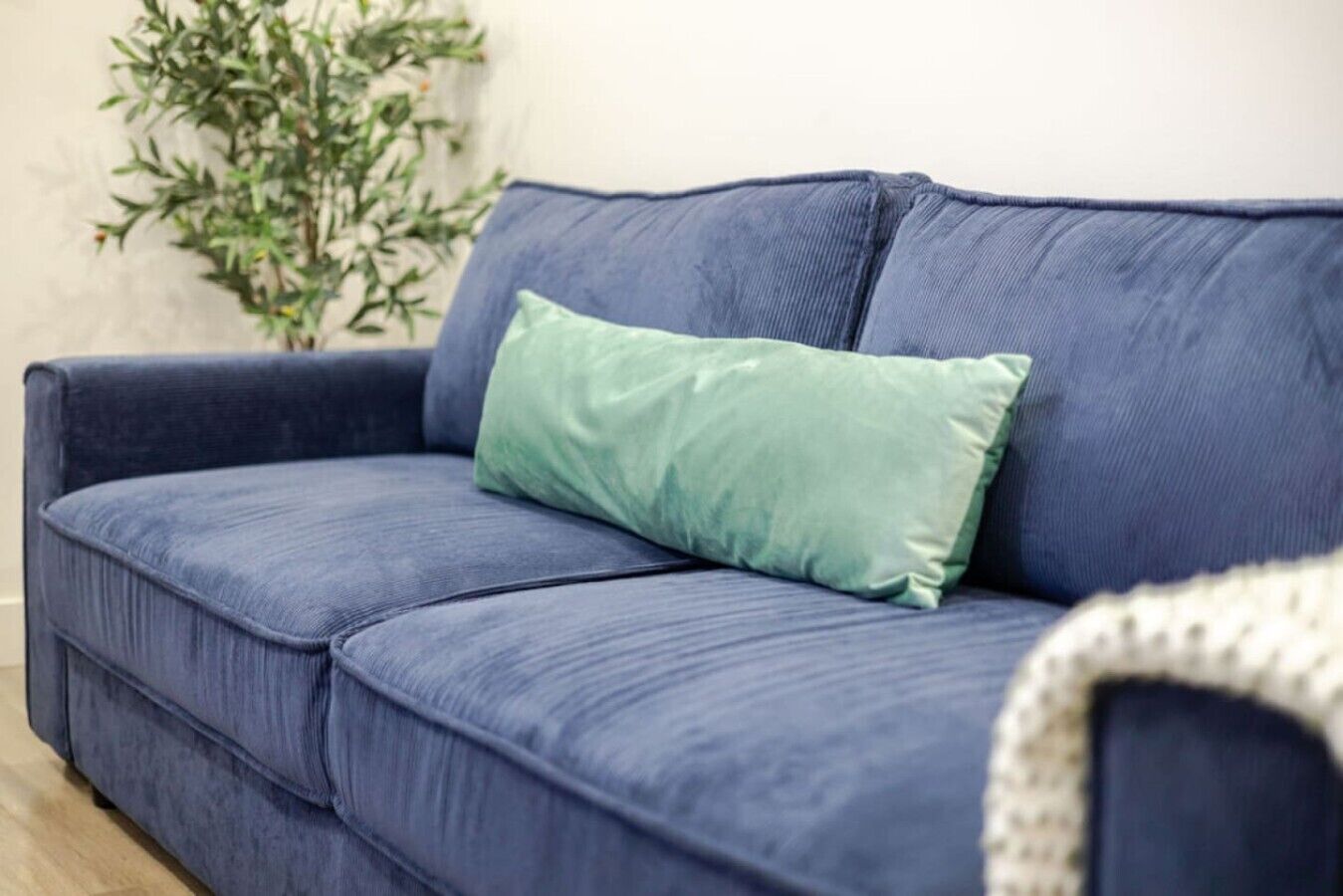 Ein blaues Sofa mit einem grünen Kissen, einer Pflanze und einer weißen Decke in einem Zimmer.
