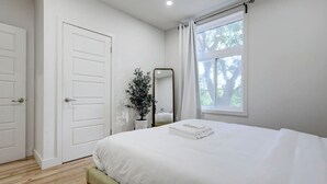 Een slaapkamer met een bed, een spiegel, een potplant en een raam.