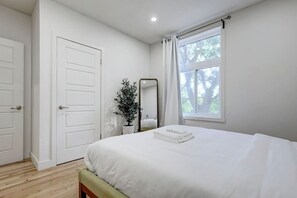 Een slaapkamer met een bed, een spiegel, een potplant en een raam.