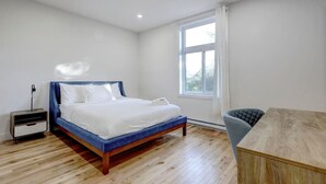 Een slaapkamer met een bed, een nachtkastje, een stoel, een raam en een houten vloer.