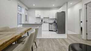 Een moderne keuken met witte kasten, een roestvrijstalen koelkast en een eethoek met een houten tafel en stoelen.