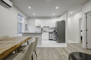 Eine moderne Küche mit weißen Schränken, einem Edelstahlkühlschrank und einem Essbereich mit einem Holztisch und Stühlen.
