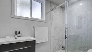 Een moderne badkamer met een glazen douchecabine, een wastafel met spiegel en een raam boven de wasbak.