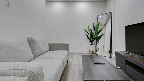 Een moderne woonkamer met een grijze bank, een donkerhouten salontafel, een flatscreen televisie en een grote spiegel.