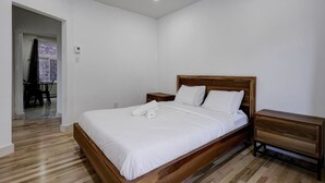 Een slaapkamer met een houten bed, witte beddengoed, een nachtkastje van hout en een houten dressoir.