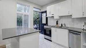 Een moderne keuken met witte kasten, een inbouwoven, een vaatwasser en een raam met uitzicht op groen.