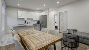 Une cuisine moderne avec des meubles blancs, une table à manger avec des chaises, un canapé gris et une petite table noire.