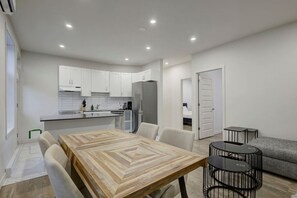 A modern kitchen with white cabinets, a dining table with chairs, a grey sofa, and a small black table. - Stylish Stay in Montréal (Montreal)