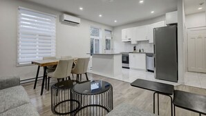 Une cuisine moderne avec des meubles blancs, un réfrigérateur et un coin repas comprenant une table et des chaises.