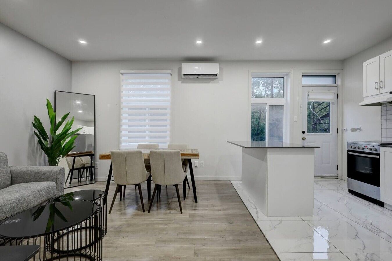A modern kitchen with white cabinetry, a dining area with a table and chairs, and a living space with a sofa and a coffee table.