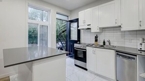 Une cuisine moderne avec des meubles blancs, une cuisinière noire et une fenêtre donnant sur un espace vert.
