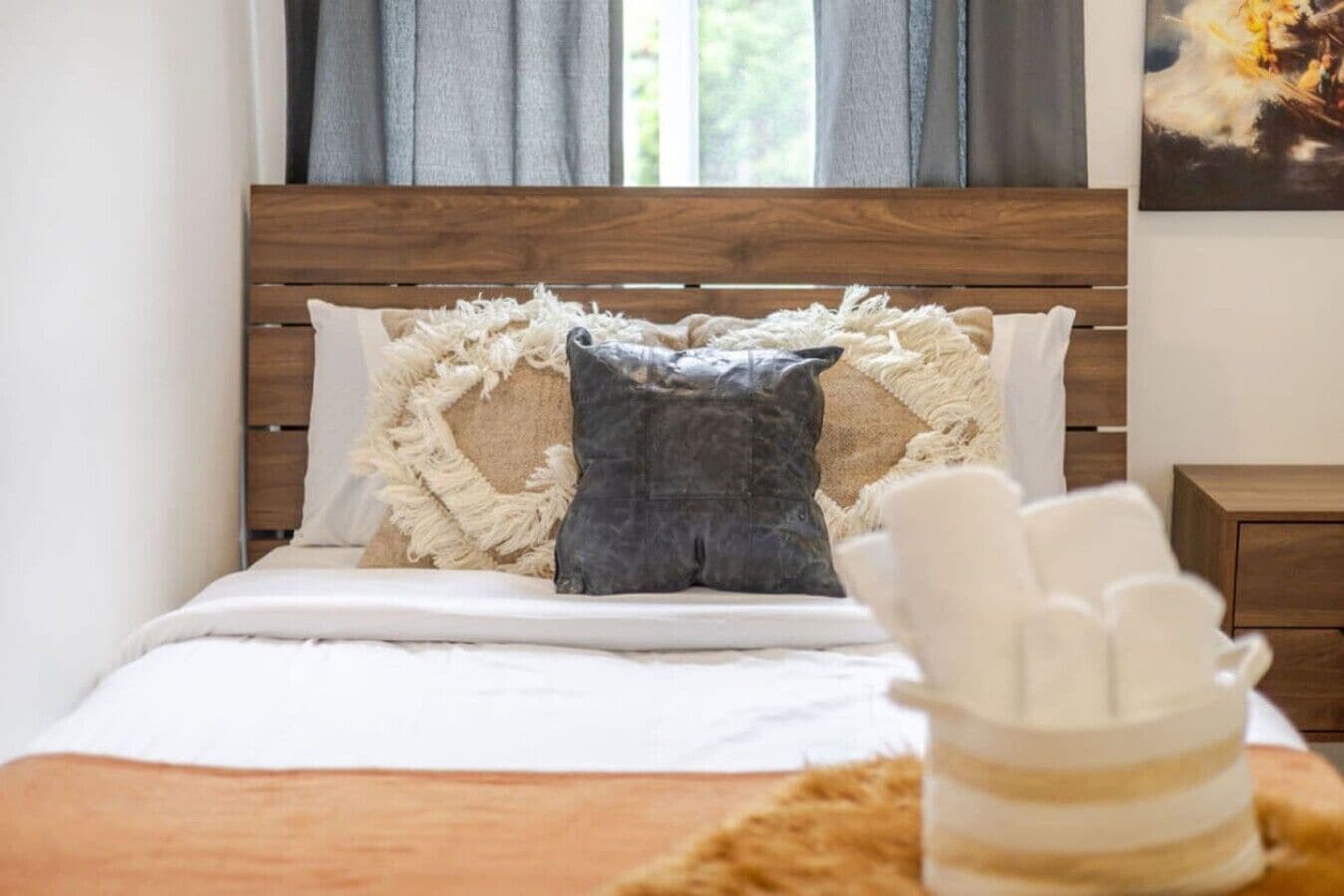 A bed with a wooden headboard, two pillows, a white blanket, and a small bedside table with a lamp.