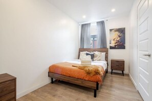 Quarto com cama de madeira, mesa de cabeceira, porta e um quadro na parede.
