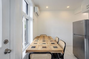 A compact kitchen with a built-in refrigerator, a dining table with chairs, and a window with blinds.