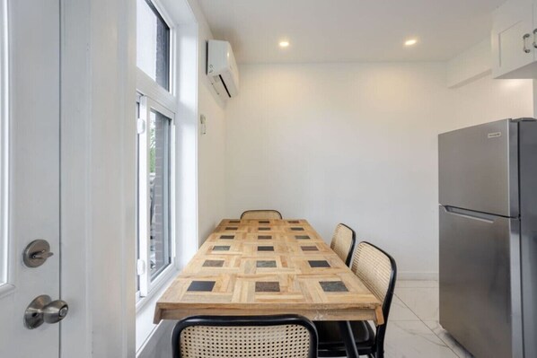 A compact kitchen with a built-in refrigerator, a dining table with chairs, and a window with blinds.
