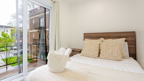 A bedroom with a large window, a wooden headboard, and a white bedspread. - Beautiful Stay in MTL (Montreal)