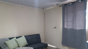 A room with a dark-colored sofa, a grey blanket, and a grey curtain. - Goly's Cabin - Sky with a View of Barú Volcano (Volcán)