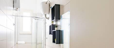 A modern bathroom with a glass shower enclosure, a white sink, and a mirror with a black frame.