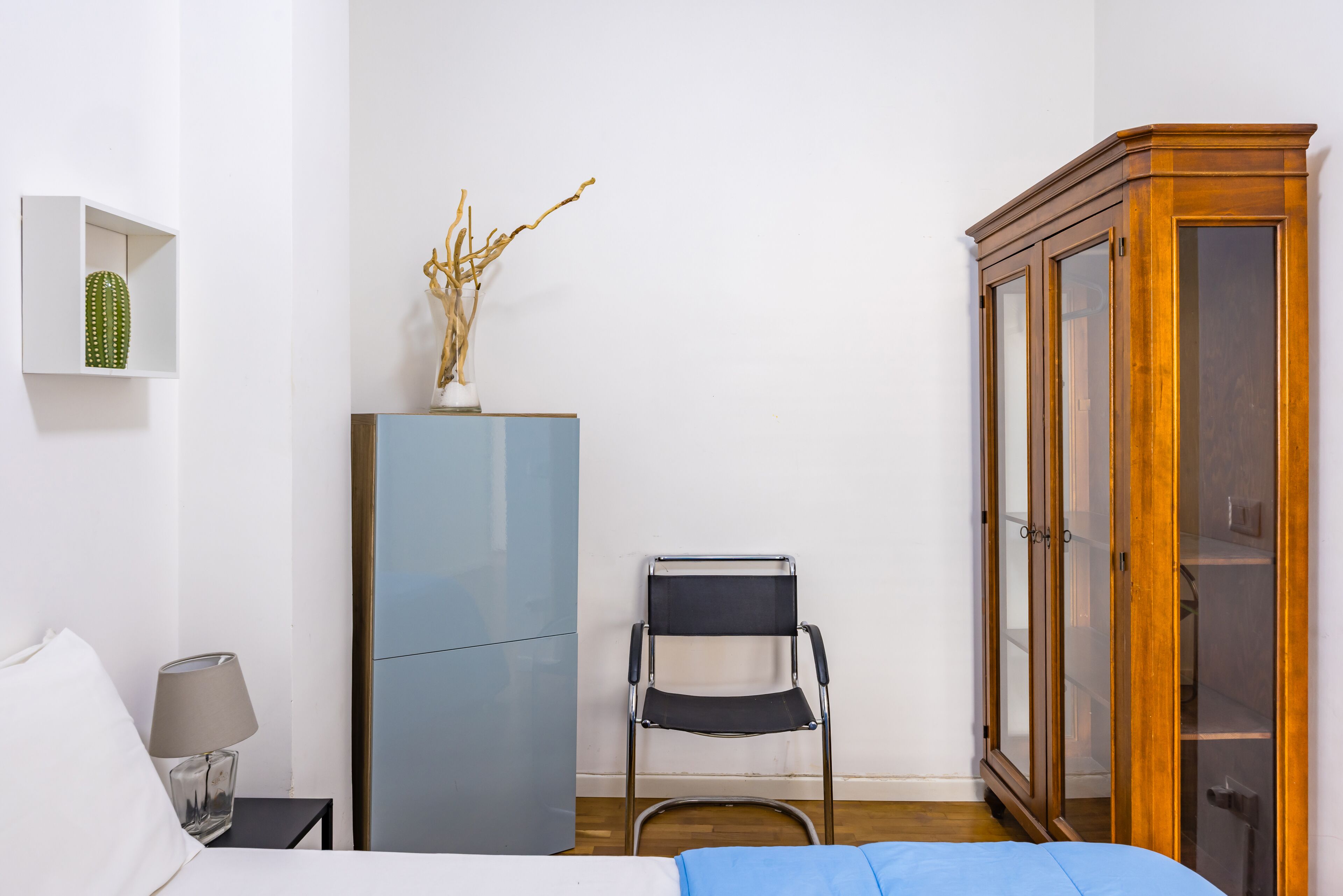 A bedroom with a bed, a nightstand, a lamp, a dresser, a chair, and a cabinet.