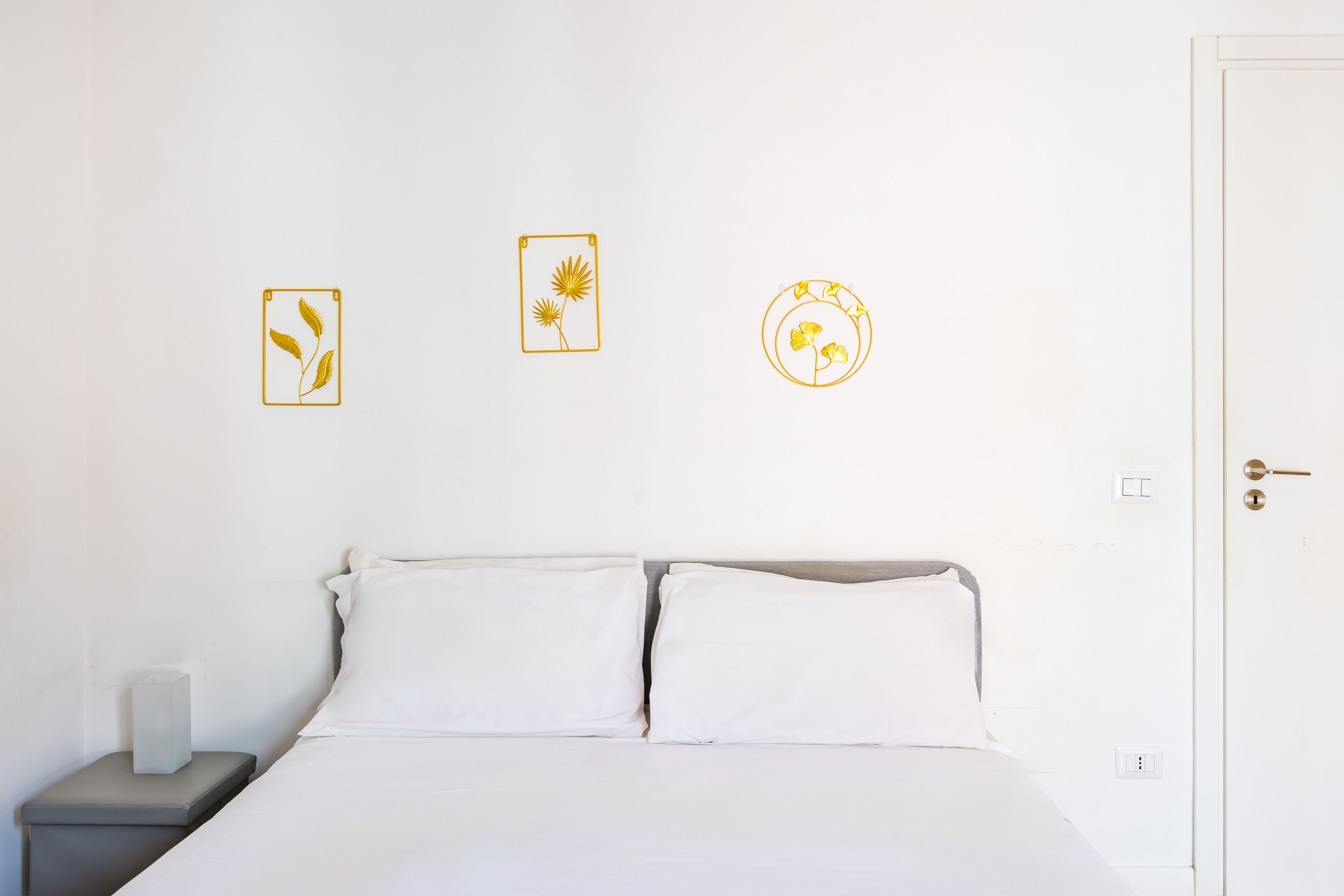 A bed with white linens, a bedside table with a lamp, and three wall art pieces.