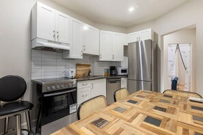 A modern kitchen with white cabinets, stainless steel appliances, a wooden dining table, and a black chair. - Perfect Stay in Montréal (Montreal)