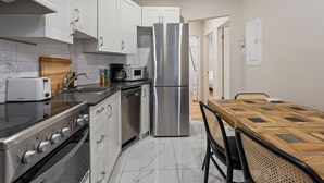Une cuisine moderne avec des meubles blancs, des appareils en acier inoxydable, une table à manger en bois et un sol carrelé.