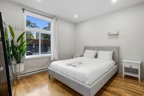 A modern bedroom with a large bed, bedside tables, a potted plant, and a window with curtains. - Perfect Stay in Montréal (Montreal)