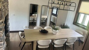 En spiseplads med et træbord, hvide stole, en væg i sten og et stort spejl.