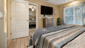 A bedroom with a bed, a dresser, a television, and a window with blinds.