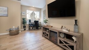 A living room with a TV, wooden flooring, a dining area, and a fireplace.