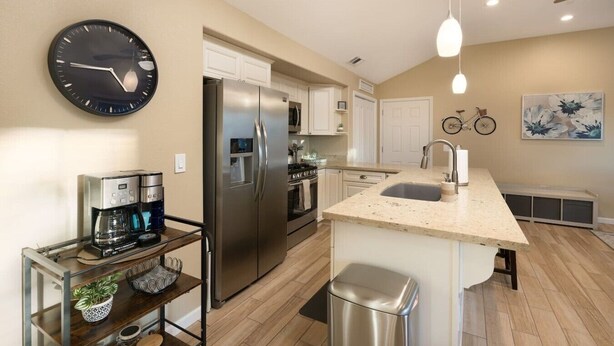 A modern kitchen with a stainless steel refrigerator, a coffee maker, and a clock on the wall.