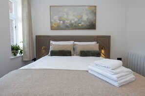 Un lit bien fait, avec une tête de lit, une fenêtre avec des rideaux et un tableau accroché au mur.