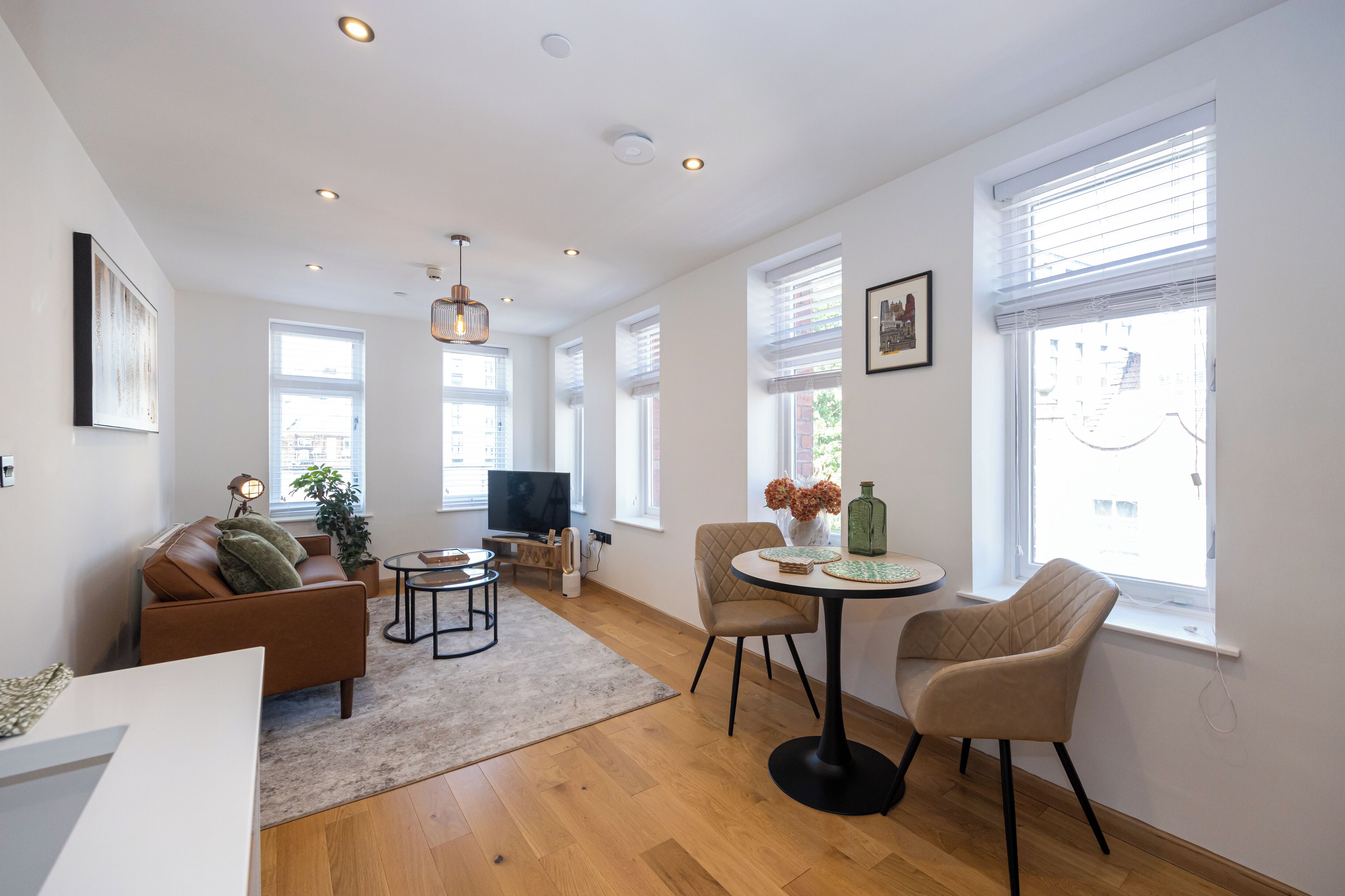 A modern living room with a sofa, chairs, a coffee table, a TV, and a large window with blinds.