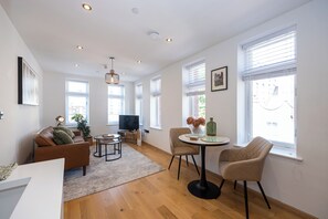 Un salon moderne comprenant un canapé, des fauteuils, une table basse, un téléviseur et une grande fenêtre avec des stores.