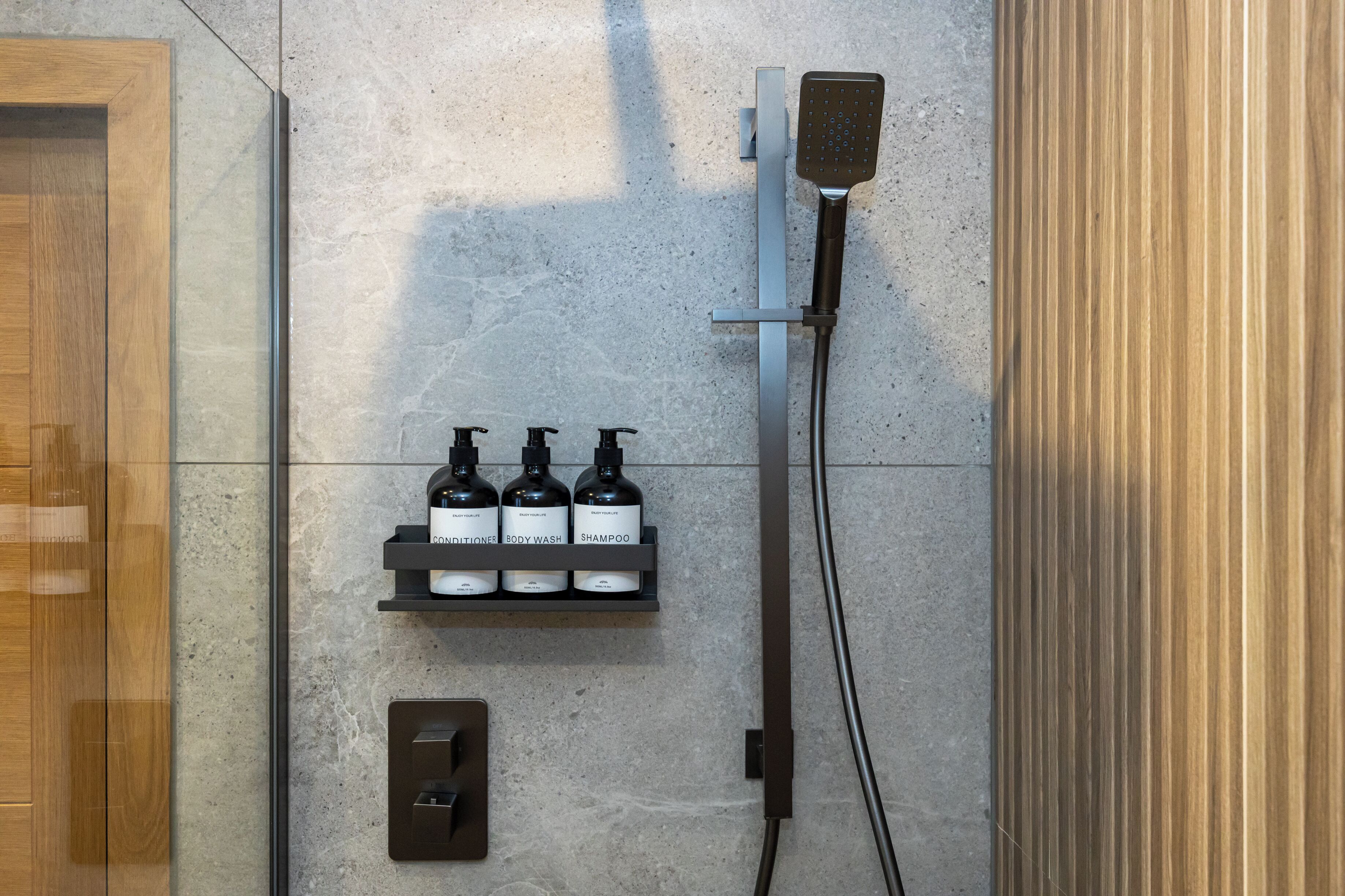 Une salle de bain moderne équipée d’une douche, d’une étagère pour le distributeur de savon et d’un panneau de commande.