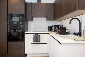 A modern kitchen with wood cabinets, a Bosch oven, a coffee machine, and a built-in dishwasher. - Modern City Centre 1BR | Walk to Leeds Station (Leeds)
