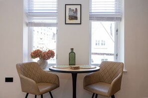 A room with two leather chairs, a round table, a vase with flowers, a framed picture, and a window with blinds. - Modern City Centre 1BR | Walk to Leeds Station (Leeds)