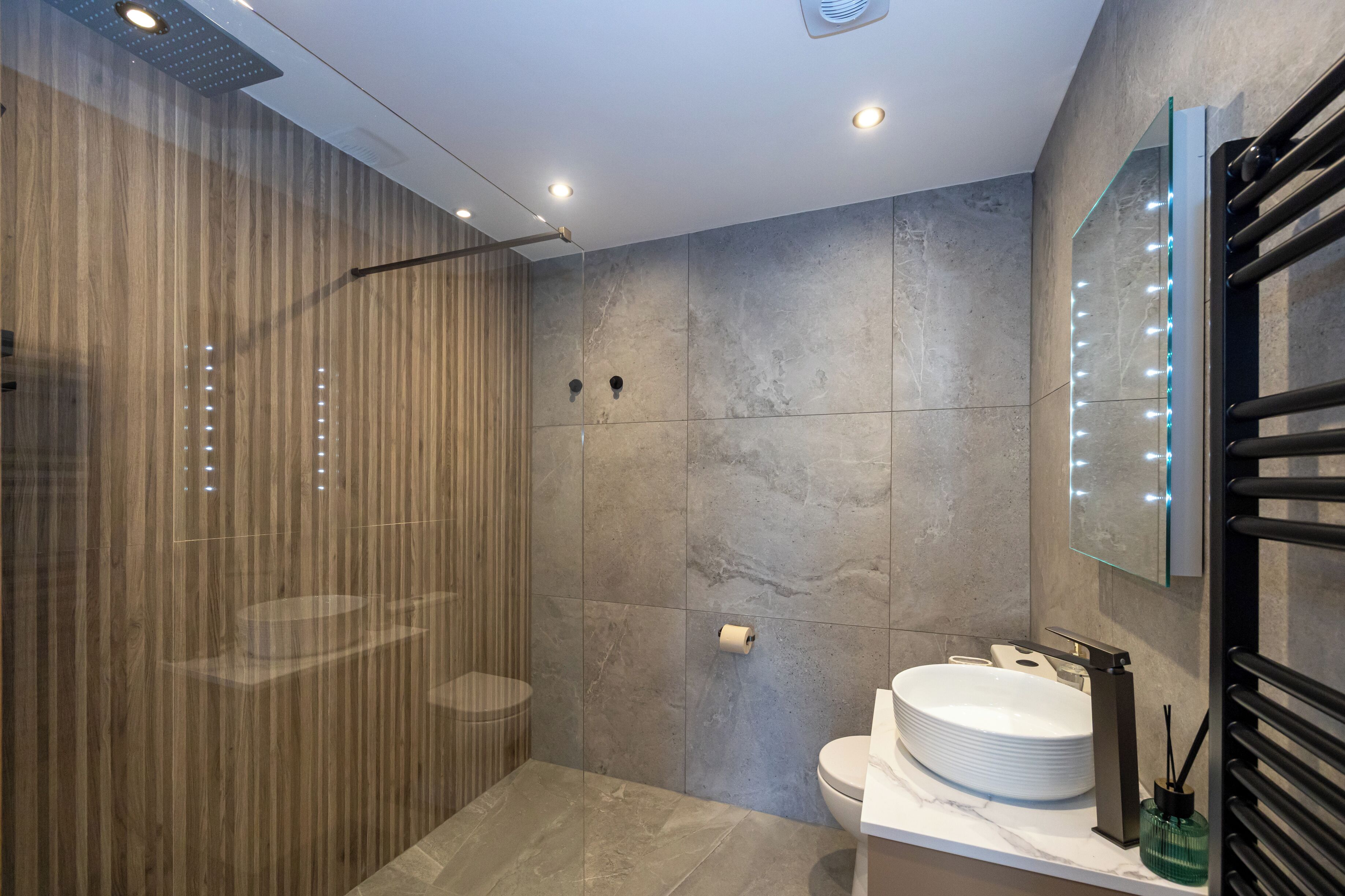 Un baño moderno con cabina de ducha de vidrio, un lavamanos blanco y un espejo con luces LED.