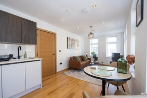 A modern kitchen with wooden cabinets, a dining area with a round table, and a living space with a sofa and a TV. - Modern City Centre 1BR | Walk to Leeds Station (Leeds)