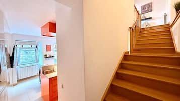 A modern kitchen with a central island, wooden staircase, and a view of the living area.