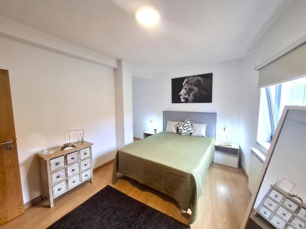 Um quarto com cama, mesas de cabeceira, cômoda, um quadro e uma janela.