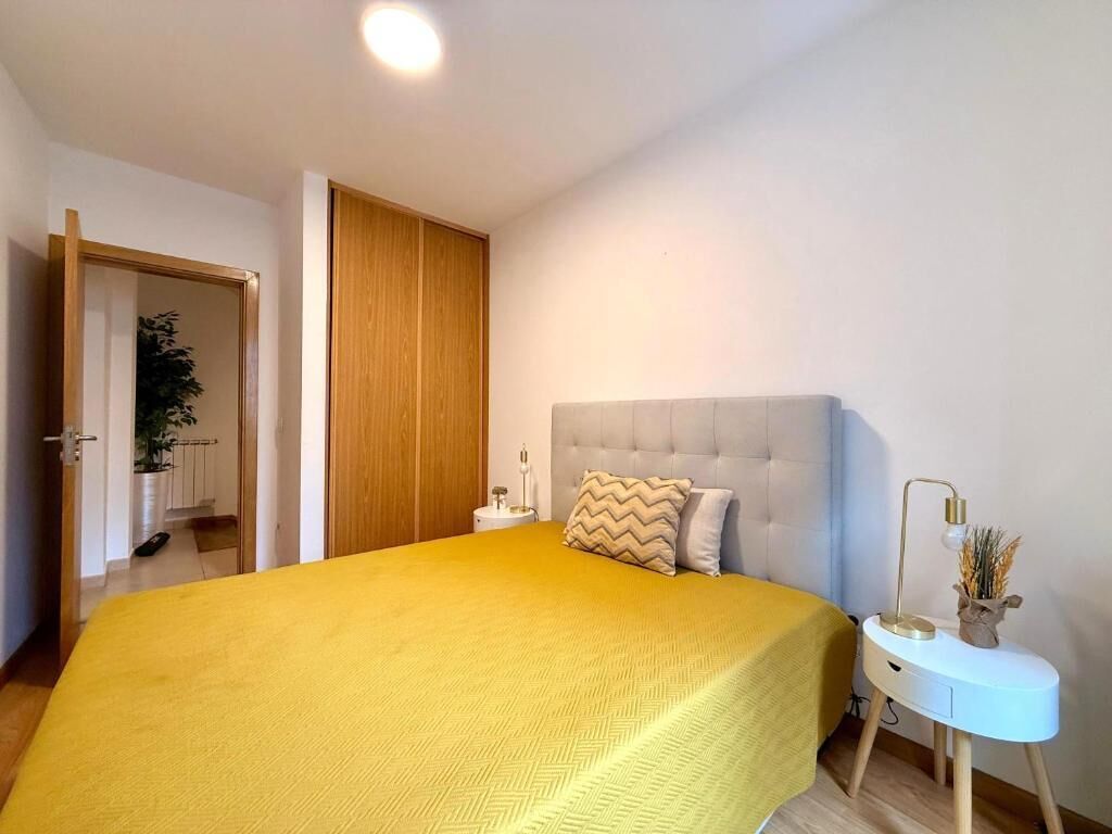 Un dormitorio con cama, mesita de noche, lámpara y una puerta que da a otra habitación.