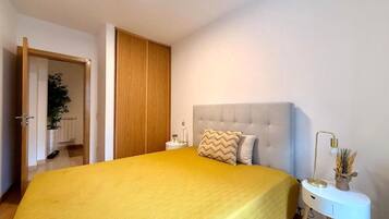 Un dormitorio con cama, mesita de noche, lámpara y una puerta que da a otra habitación.