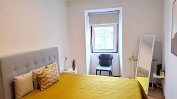 Un dormitorio con cama, una silla, un escritorio y una ventana.