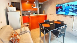 Un espacio habitable compacto con kitchenette, comedor y televisor montado en la pared.
