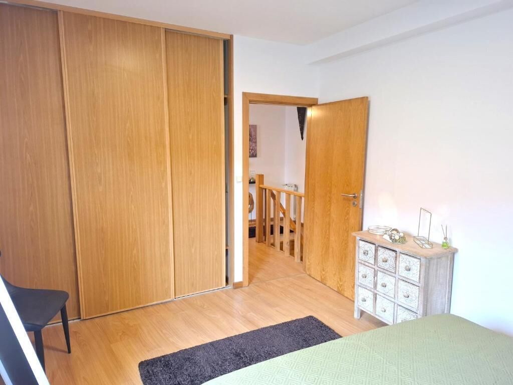 Een slaapkamer met een bed, een kapstok, een kledingkast en een trap naar een andere kamer.